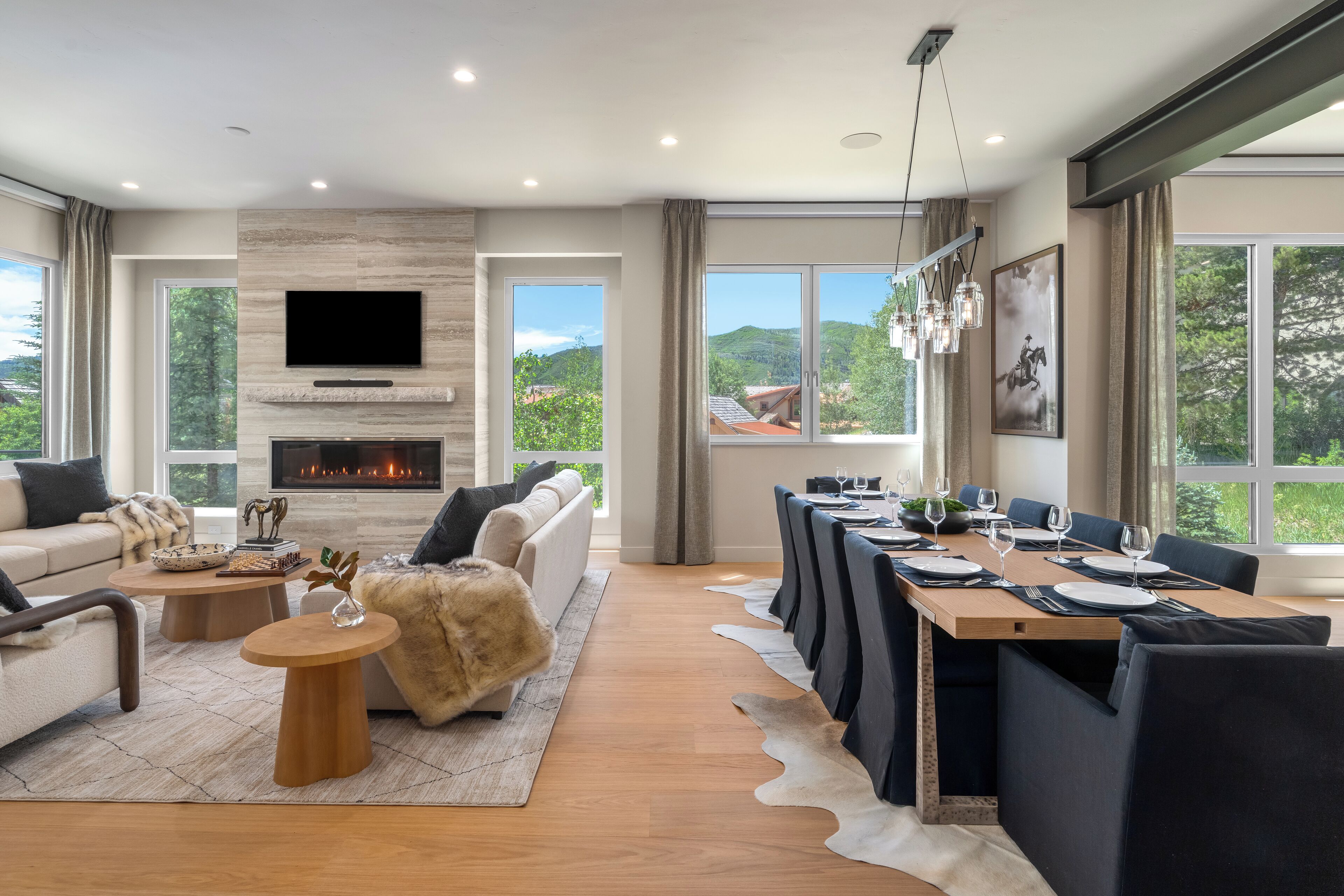 A modern living room with a fireplace, a television, and a dining area with a view of the outdoors.