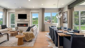 A modern living room with a fireplace, a television, and a dining area with a view of the outdoors.