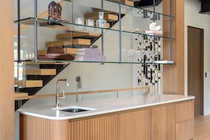 A modern kitchen with a built-in sink, wooden cabinetry, and a glass shelf displaying various items. - Close to Ski Townhome 1096 (Steamboat Springs)
