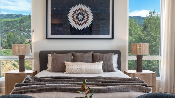 A bedroom with a large bed, two side tables, a framed artwork above the bed, and a view of the outdoors through the windows. - Close to Ski Townhome 1096 (Steamboat Springs)
