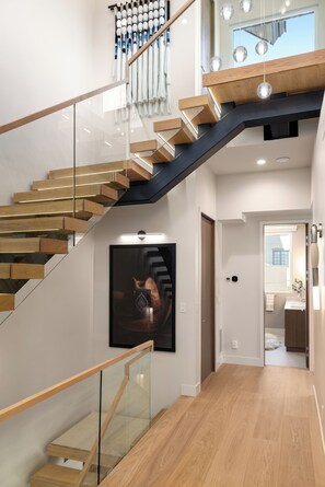 Een moderne trap met glazen balustrades en houten treden, leidend naar een tweede verdieping met uitzicht op de lucht.