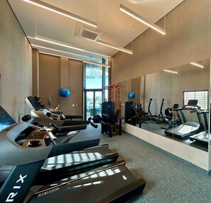 Une salle de sport équipée de machines d’exercice, d’un tapis de course et d’un mur recouvert de miroirs.