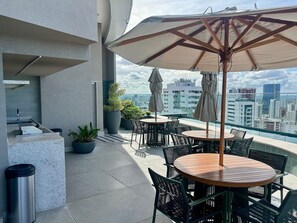 A rooftop terrace with outdoor seating, potted plants, and a view of the city skyline. - Studio de luxo no Praia de Gameleira (Recife)
