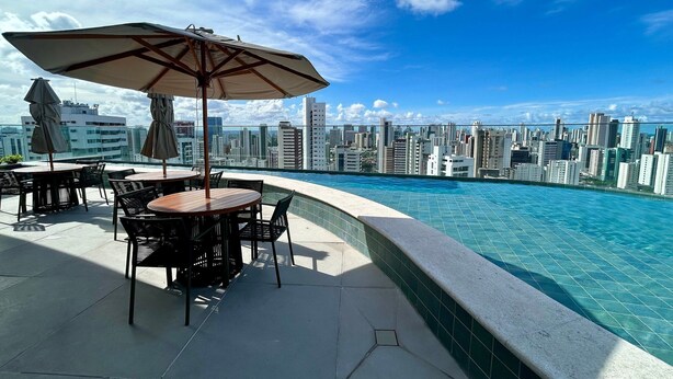 Un área de piscina en la azotea con vistas al horizonte urbano, mobiliario exterior y cielo despejado.