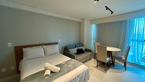 Habitación de hotel con cama, escritorio y una silla. Se aprecia una ventana con cortinas.