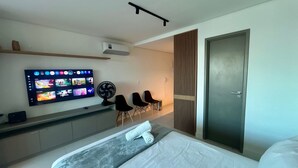 Habitación de hotel moderna con cama, televisor de pantalla plana en la pared, escritorio con ventilador y puerta corredera.