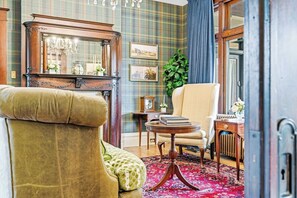 A traditional room with a large mirror, a green plaid wall, a green armchair, a wooden side table, and a red patterned rug. - Historic 1910 Pittsburgh Victorian  (Pittsburgh)