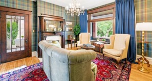 A room with a fireplace, a sofa, a chair, a table, and a large window with curtains. - Historic 1910 Pittsburgh Victorian  (Pittsburgh)