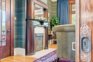 A room with a fireplace, a green plaid wall, and a patterned rug. - Historic 1910 Pittsburgh Victorian  (Pittsburgh)