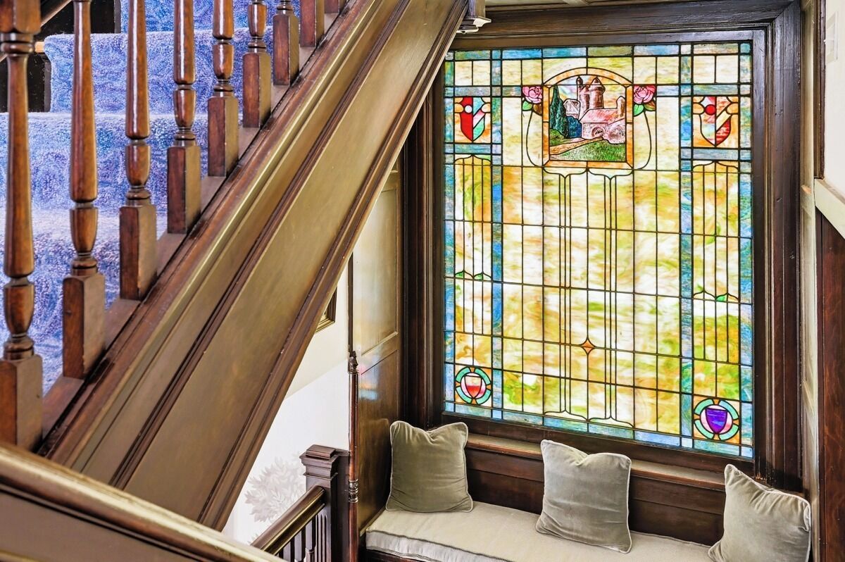 A stained glass window with geometric patterns and a bench with cushions.