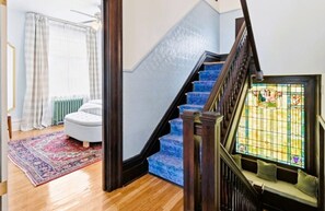 Eine Treppe mit blauen Stufen, ein Heizkörper, ein weißer Hocker und ein gemustertes Teppich.