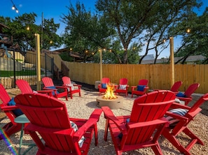 An outdoor seating area with red Adirondack chairs around a fire pit, surrounded by a wooden fence and trees. - Wildlight House: Cascade | Canyon Lake | Sleeps 17 (Canyon Lake)