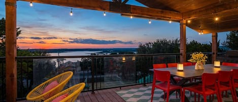 Un espace extérieur abrité, doté d’un plafond en bois, d’une balustrade en verre, d’une table avec des chaises et offrant une vue sur le paysage.