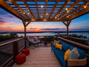 A covered outdoor seating area with a view of the water, wooden deck, and a sofa with cushions. - Wildlight House: Cascade | Canyon Lake | Sleeps 17 (Canyon Lake)