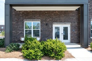 A modern building with a brick facade, two windows, a door, and a covered porch area with two chairs. - Chic, New Apt | Pool | Long Stays (Athens)