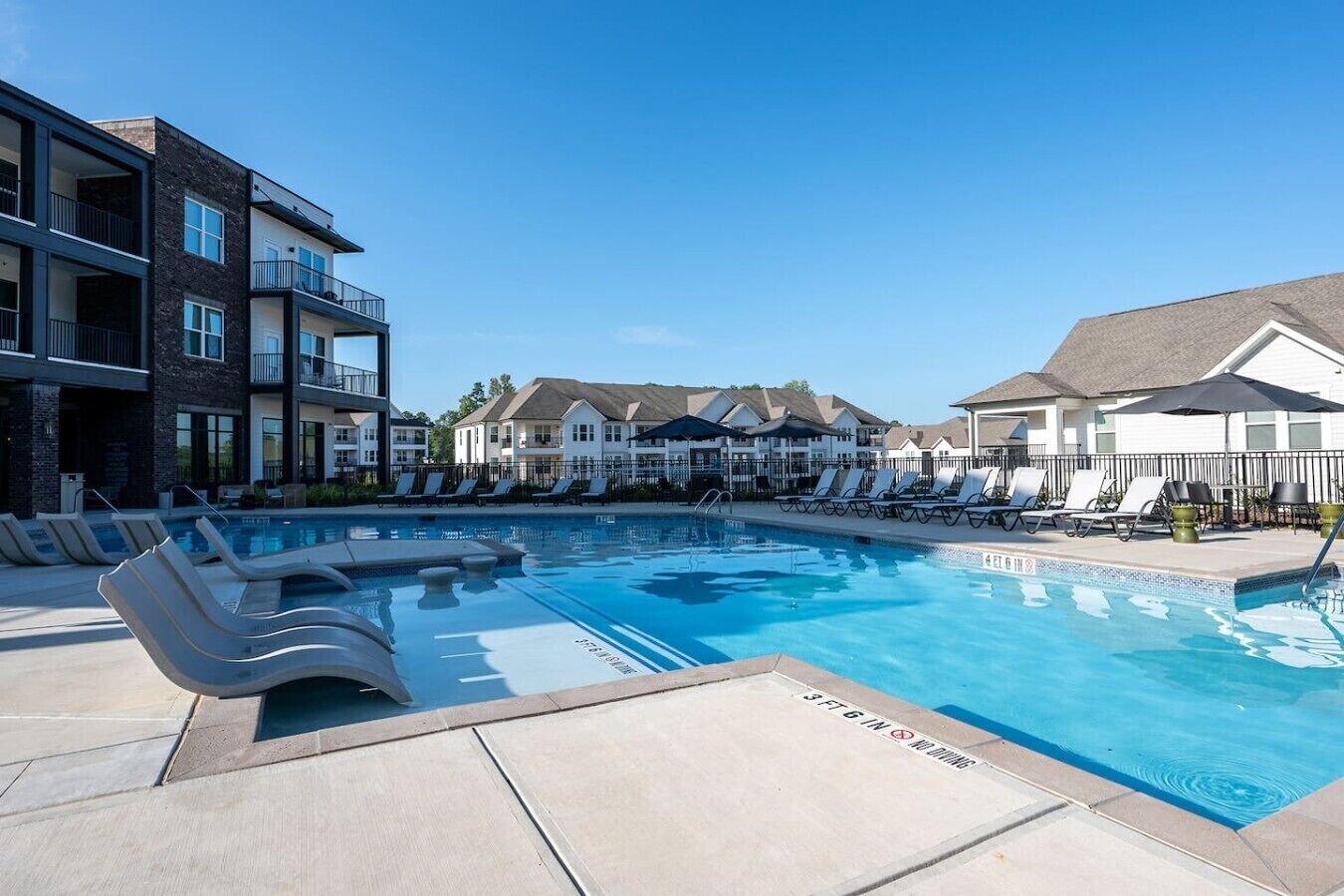 A swimming pool with lounge chairs and a building with balconies.