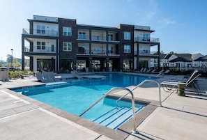 A modern multi-story building with a swimming pool, outdoor seating, and a clear sky. - Chic, New Apt | Pool | Long Stays (Athens)