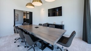 Uma sala de conferências com uma mesa comprida, cadeiras e iluminação pendente.