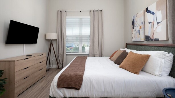 Quarto de hotel com cama, televisão, mesa de cabeceira, abajur e obras de arte na parede.