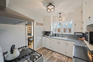 A modern kitchen with a gas stove, white cabinets, a welcome sign, and a window with curtains. - Cozy 4-bedroom home in Cheyenne close to Frontier/Lions Park and downtown (Cheyenne)