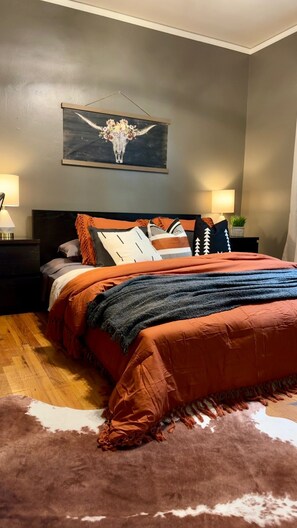A bedroom with a bed, nightstands, a wall-mounted painting, and a rug.