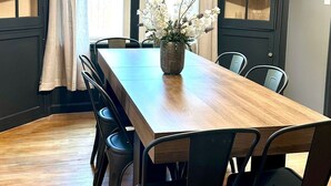 Ein Esszimmer mit einem langen Holztisch, schwarzen Stühlen, einer Vase mit Blumen und einer Kristallleuchter.
