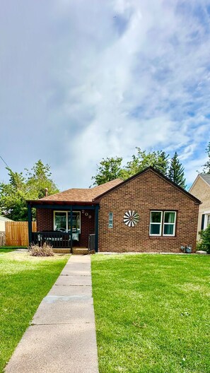 A single-story brick house with a front porch, a mailbox, and a large clock on the side.