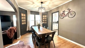 Een eethoek met een houten tafel, stoelen, een kroonluchter en een fiets aan de muur.