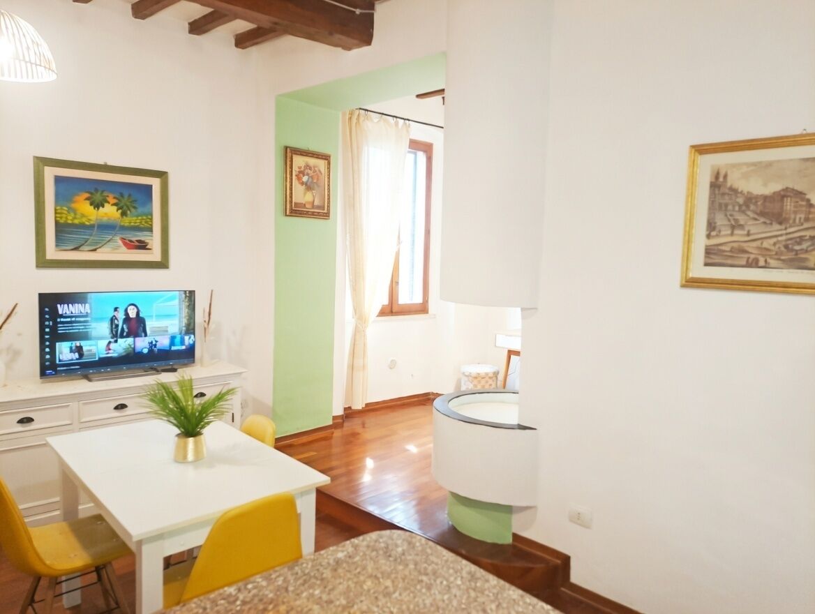 Una habitación con televisión, una mesa de comedor con sillas, una planta y obras de arte en las paredes.