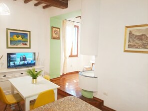 Habitació amb televisió, taula de dinar amb caires, una planta i obra d'art a les parets.