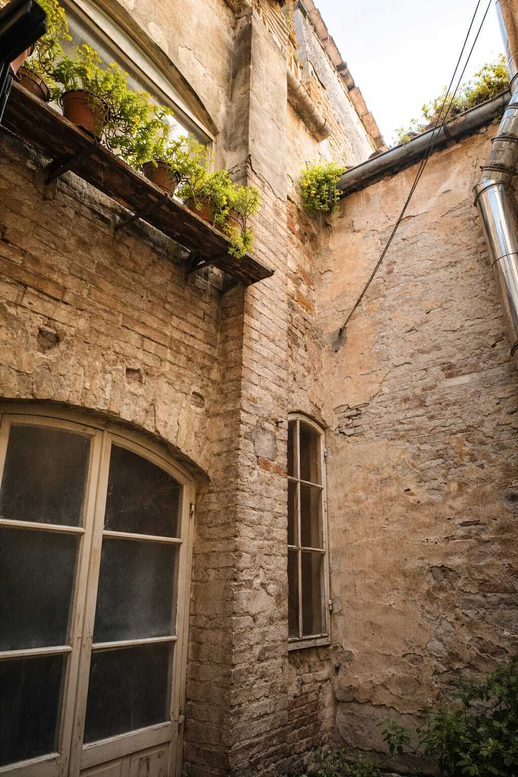 Un estrecho callejón con un edificio de ladrillo, una ventana con contraventana de madera y un ventanal con marco de madera.