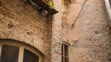 Un estrecho callejón con un edificio de ladrillo, una ventana con contraventana de madera y un ventanal con marco de madera.