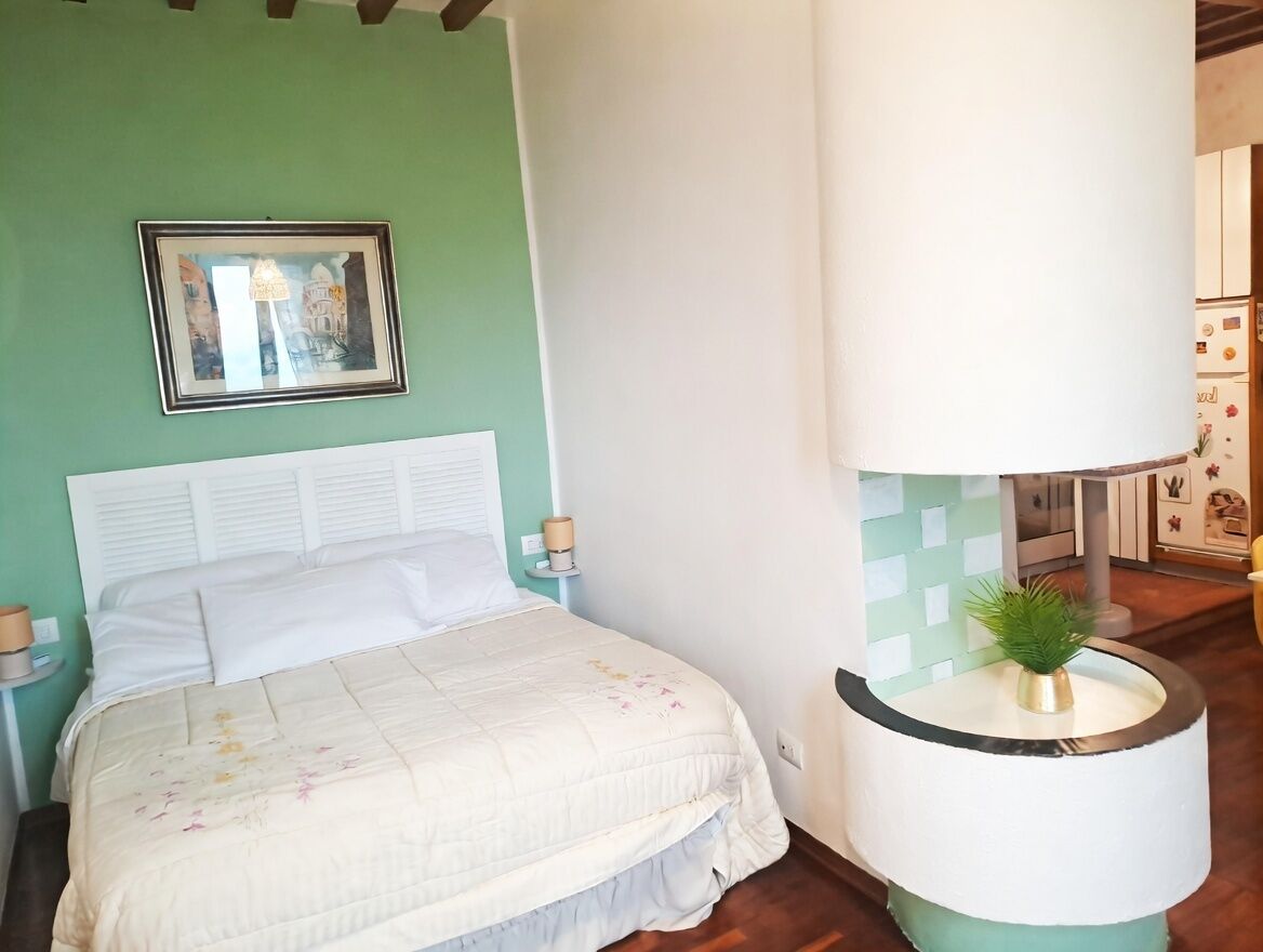Une chambre à coucher avec un lit, une lampe de chevet, un tableau encadré au mur et une petite plante sur une table.