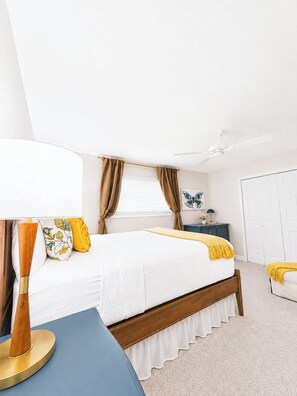 A bedroom with a bed, a bedside table, a lamp, a window with curtains, a ceiling fan, and a door. - The Cali Belle, Walk to Campus by Velvet Ditch Villas (Oxford)