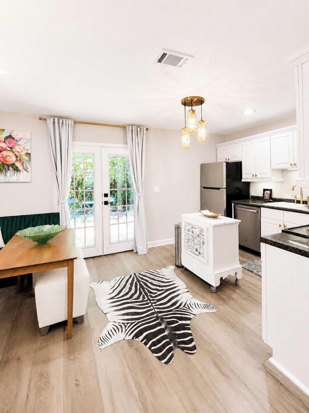 A modern kitchen with white cabinets, a black refrigerator, and a dining area with a wooden table and a zebra print rug.
