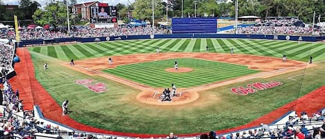 A baseball stadium with a large audience, a baseball diamond, and a stage for events.