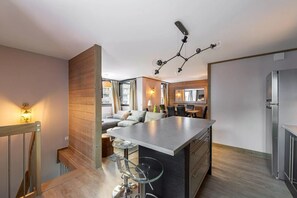 A modern kitchen with a central island, a dining area with a table and chairs, and a seating area with a sofa. - Solaise 202–302 – Stunning Renovated Duplex in the Heart of Val d’Isère (Val-d'Isère)