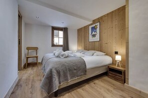 Ein Schlafzimmer mit Holzkopfteil, einem Bett mit weißer Bettwäsche, einem Nachttisch mit Lampe und einem Fenster mit Vorhängen.