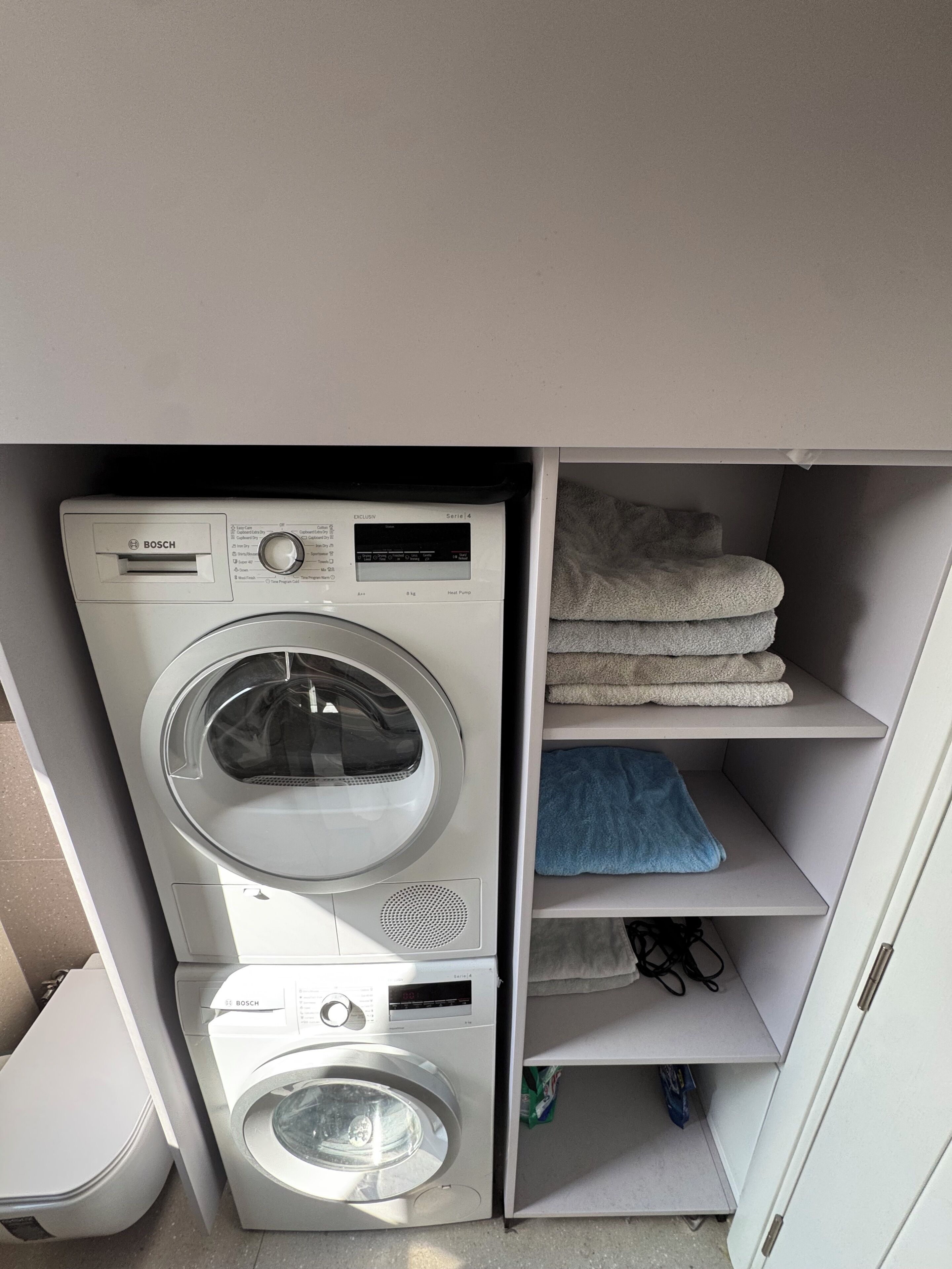 Un espace buanderie compact comprenant deux machines à laver Bosch superposées et une étagère avec des serviettes pliées.