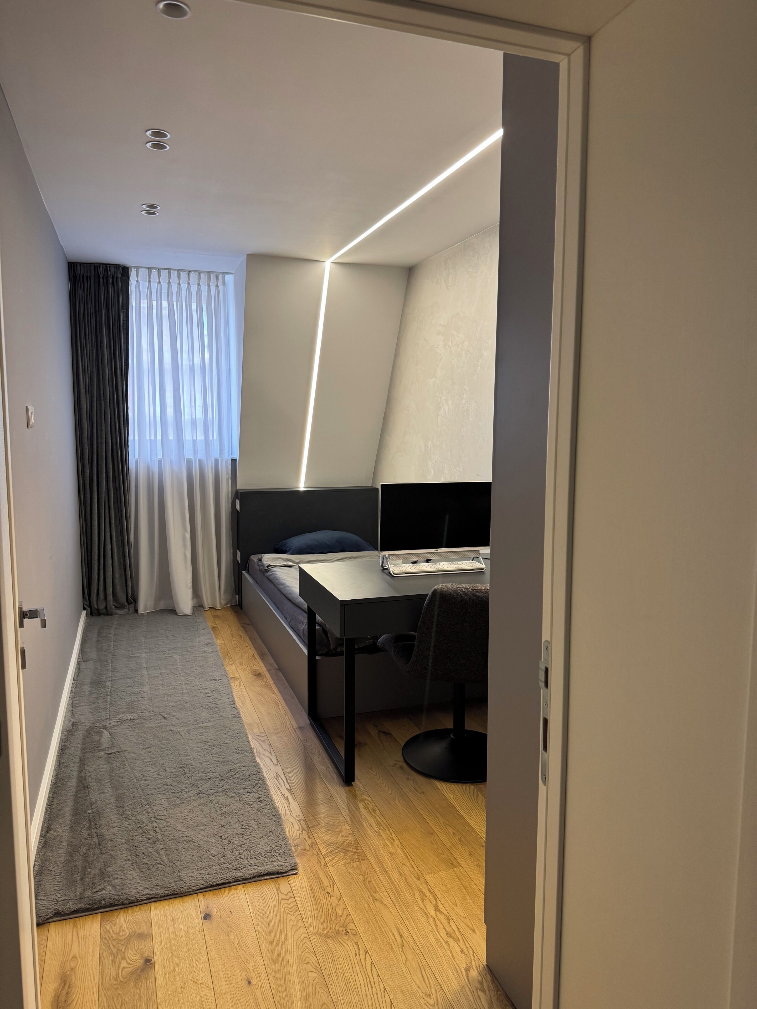 Un dormitorio moderno con cama, escritorio y computadora.
