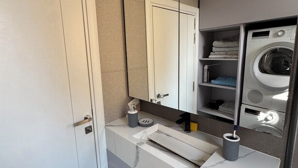 Un baño moderno con una puerta blanca, un lavabo de mármol, un espejo integrado y una lavadora empotrada.