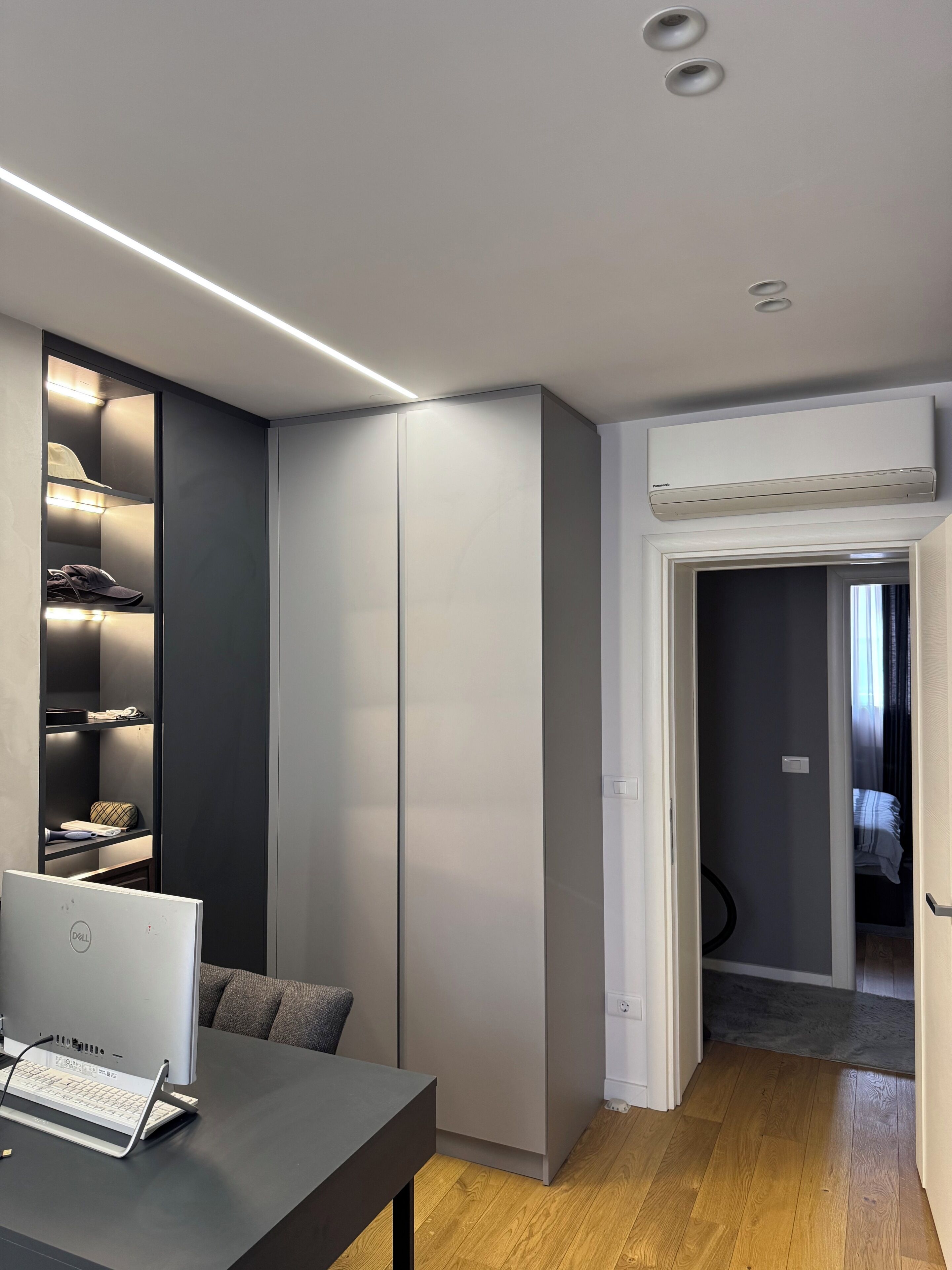 Une chambre moderne équipée d’un bureau, d’un ordinateur et d’une armoire avec des étagères éclairées.
