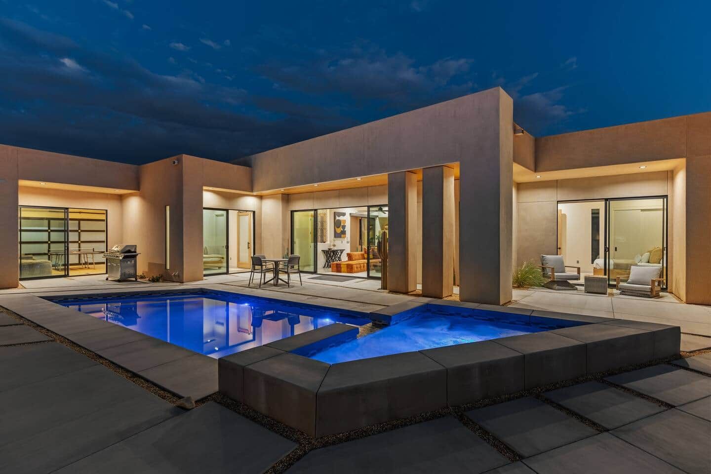A modern outdoor pool area with a patio, seating, and a glass-enclosed living space.
