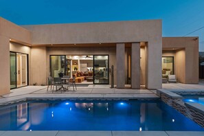 A modern house with a swimming pool, a patio with outdoor furniture, and a glass door leading to an interior space.