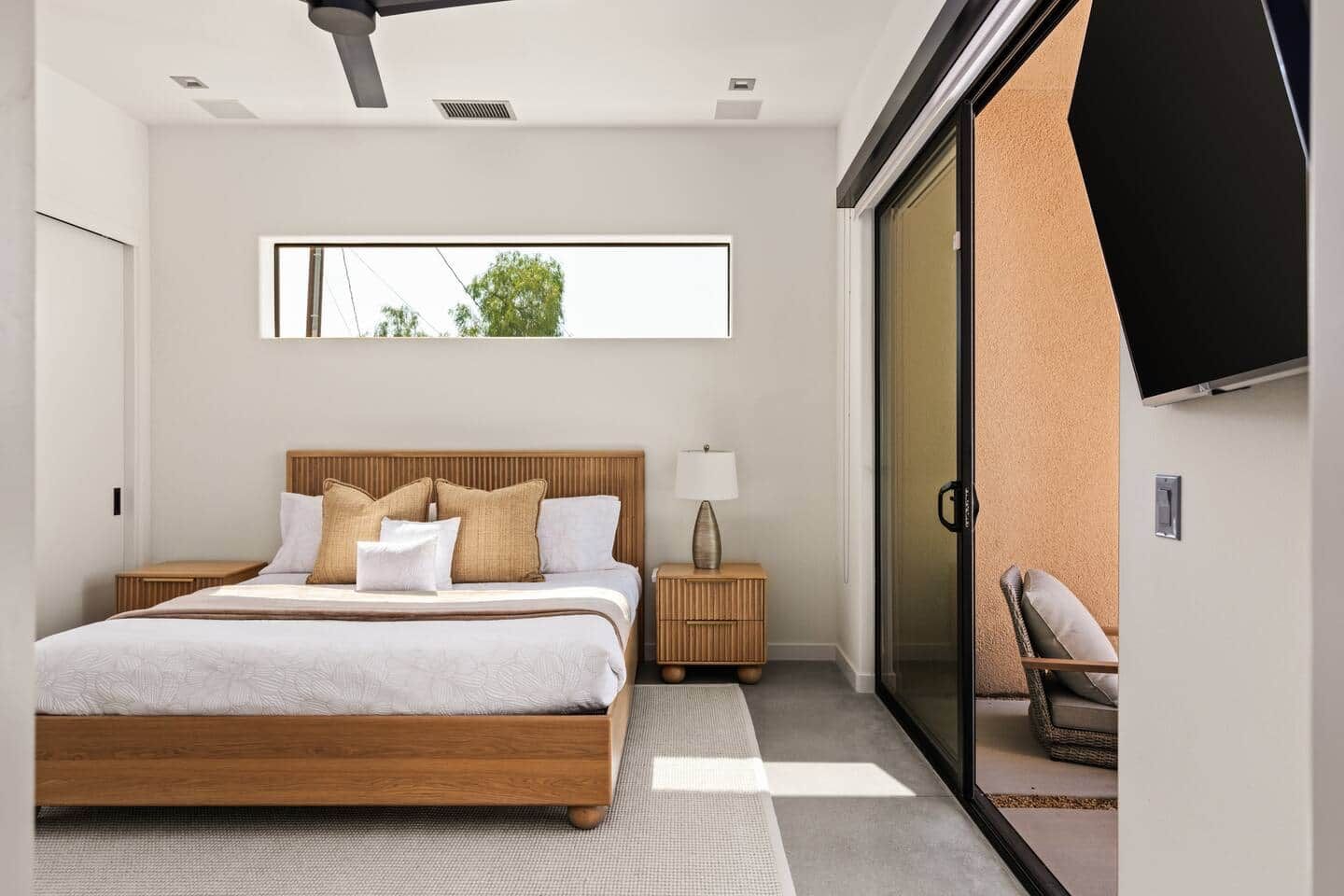 A modern bedroom with a large bed, bedside tables, a TV, and a sliding glass door leading to a balcony.