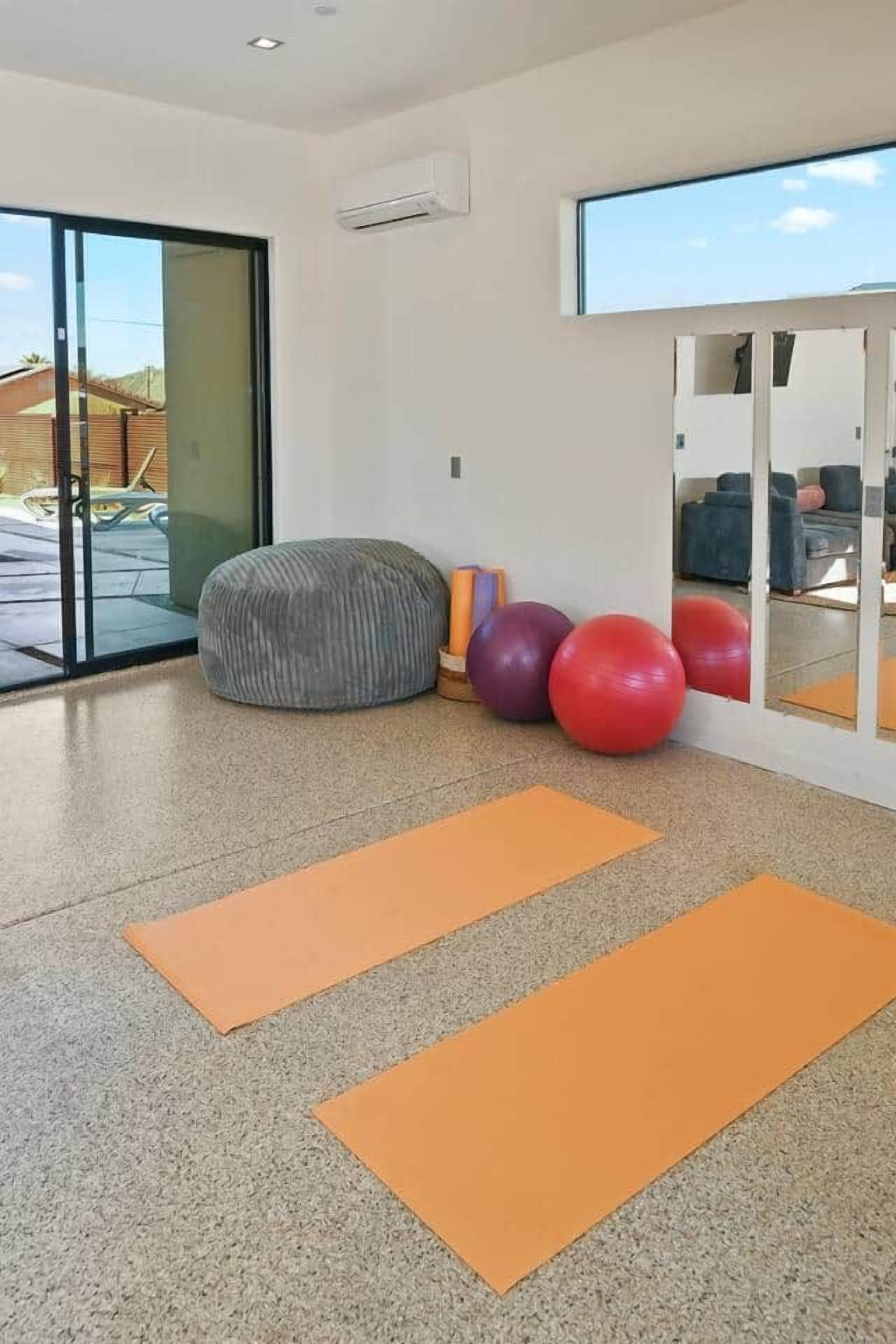 A spacious room with a large sliding glass door leading to an outdoor area, a grey bean bag chair, several exercise balls, and orange yoga mats.