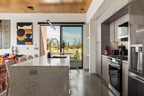 Une cuisine moderne dotée d’un îlot central, d’appareils électroménagers en acier inoxydable et offrant une vue sur l’extérieur.