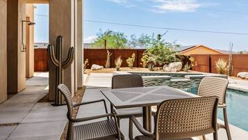 A poolside area with a table and chairs, a cactus, and a wooden fence.