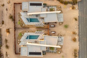 A modern hotel with multiple swimming pools, outdoor seating areas, and a desert landscape.