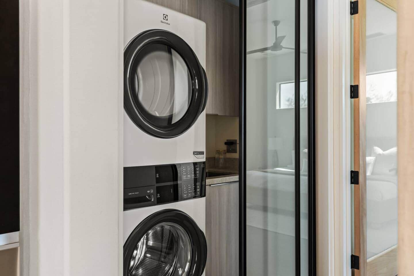 Un lavadero moderno con dos lavadoras y una puerta de cristal que da a un dormitorio.